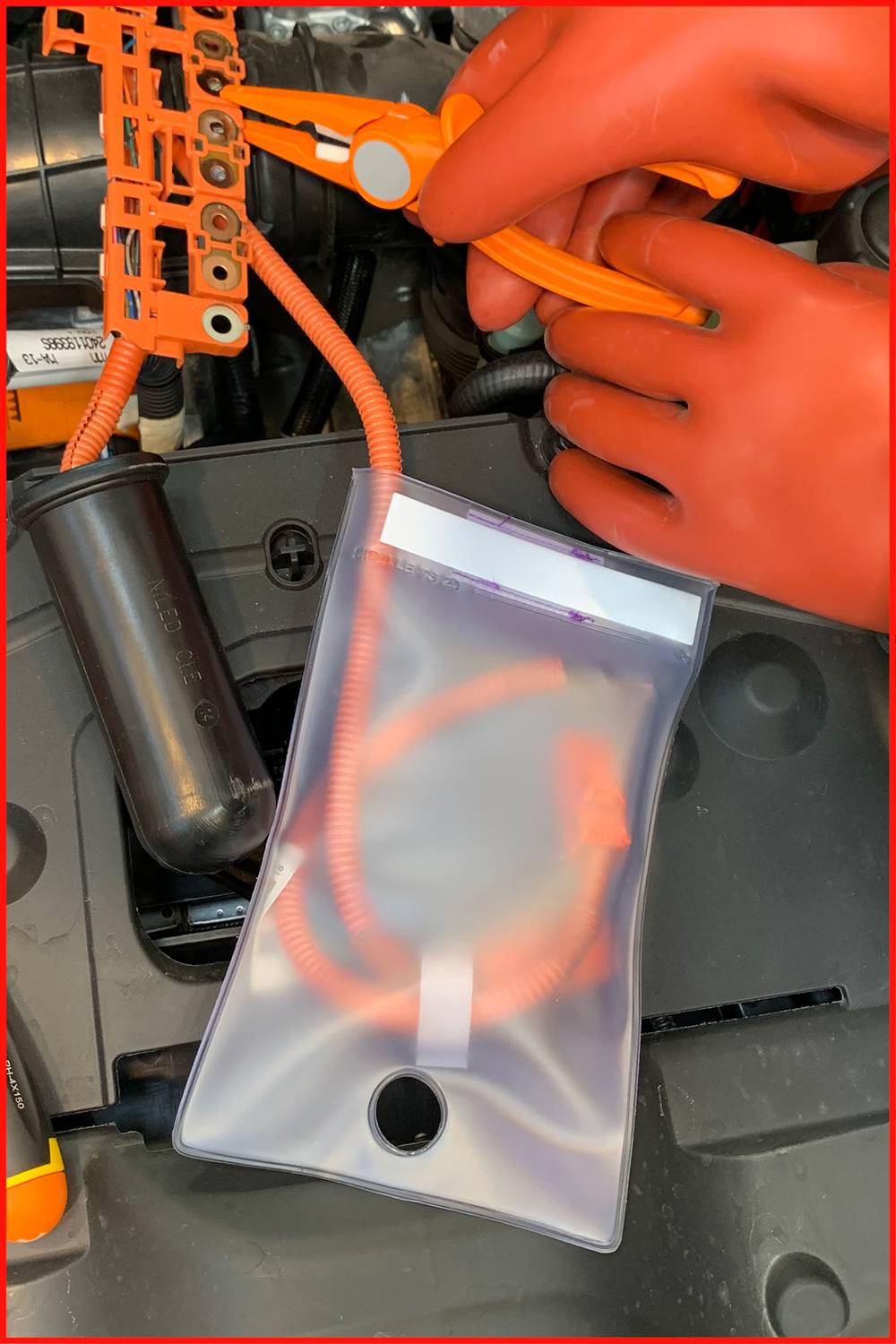 Handen van een monteur met rode handschoenen werken in een auto aan een elektrische kabelboom naast een transparante beschermhoes.