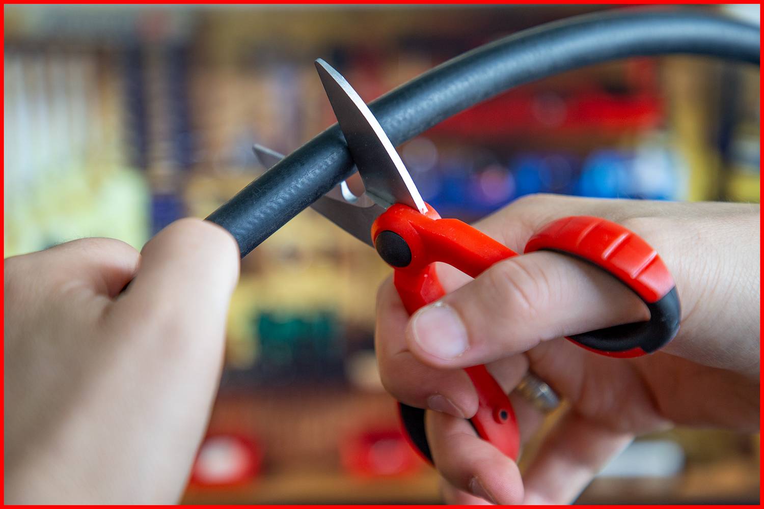 Handen knippen een zwart kabel met een rode schaar voor een wazig achtergrond.