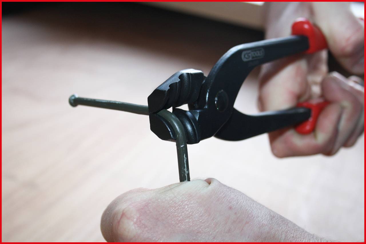 Een persoon gebruikt een boutenschaar met rode handvatten om een draad door te knippen. De achtergrond is wazig.