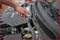 Persoon repareert motorruimte van een auto met een schroevendraaier, close-up van hand en motorruimtedetails.