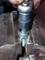 Close-up van een metalen tang die een schroef vasthoudt, terwijl een hand met een ratelgereedschap de moer aanhaalt.