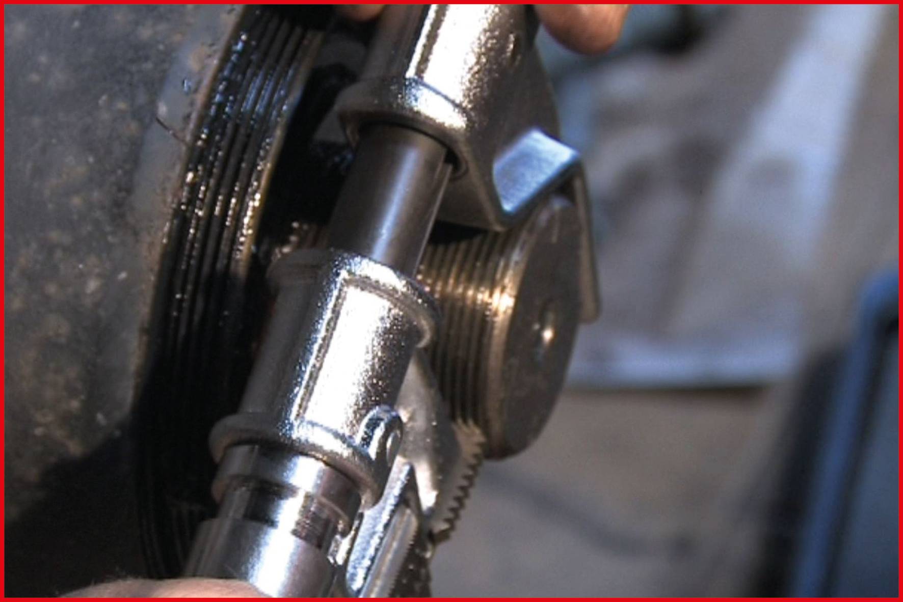 Close-up van een pijptang die een metalen staaf vasthoudt. De scène toont een ambachtelijke activiteit in een werkplaatsomgeving.