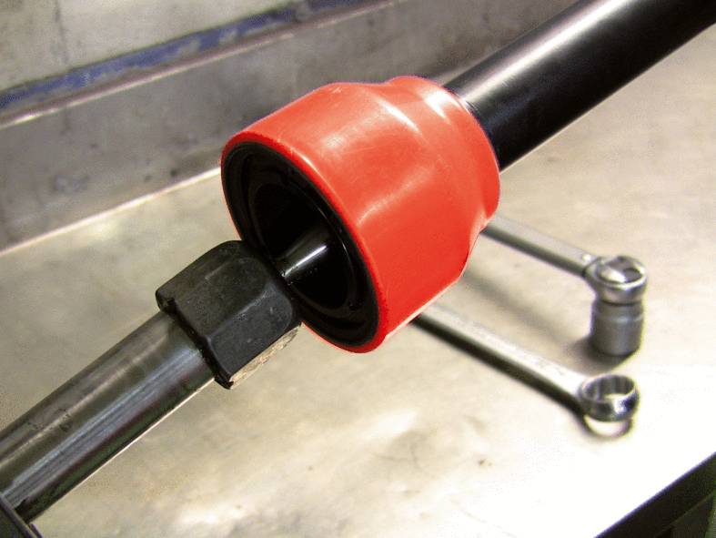 Close-up van een zwart metalen buis met rode kunststof coating, bevestigd in een mechanische constructie, met gereedschappen op de achtergrond.