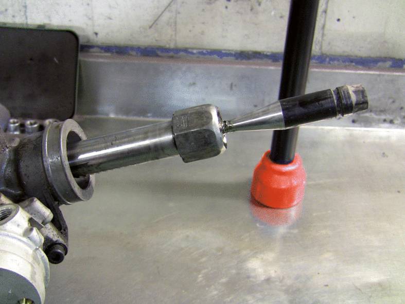 Een metalen gereedschap met een lange steel ligt op een werkbanktafel. Het lijkt deel uit te maken van een machinebouwonderdeel.