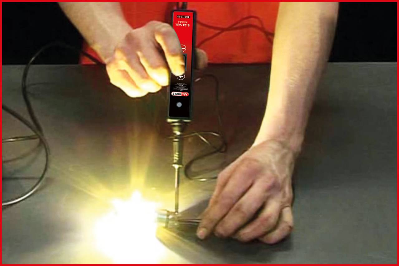 Een persoon gebruikt een soldeerbout om een metalen onderdeel te solderen met een lichtgevend punt. De omgeving is donker, met de focus op de handen.