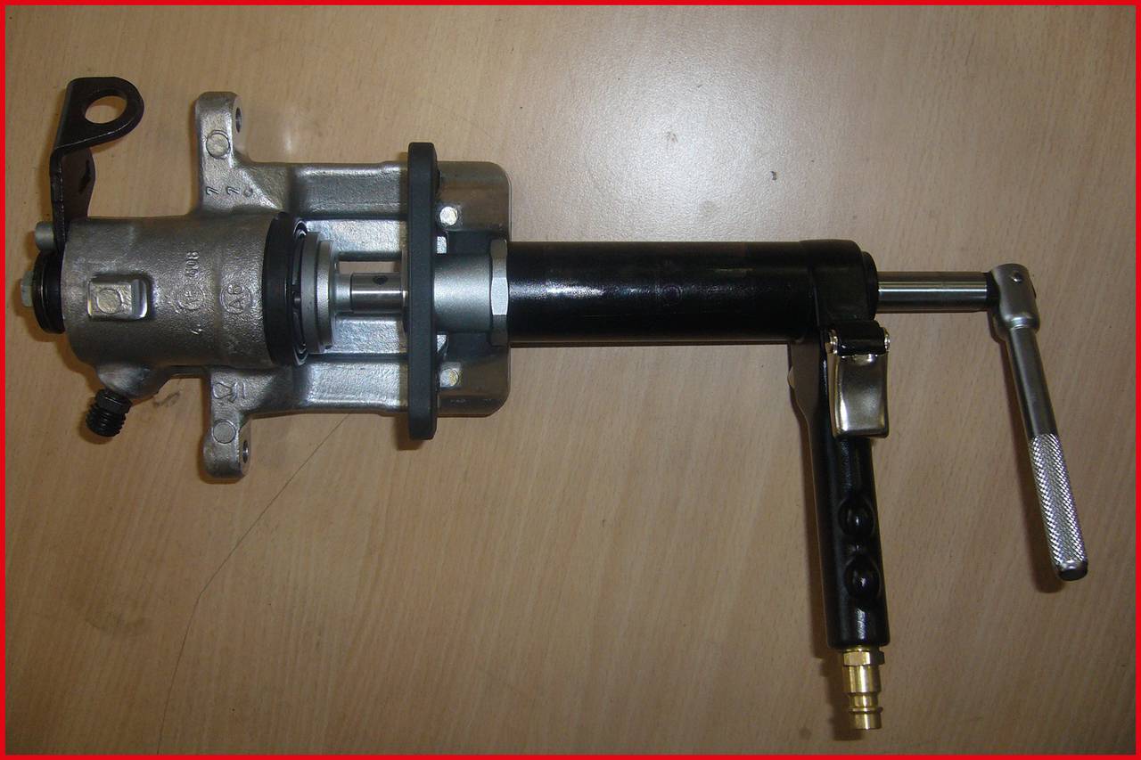 Hydraulische voorziening op een houten tafel. Beschikt over een handgreep, zuiger en hefboom, vermoedelijk voor industriële toepassingen.