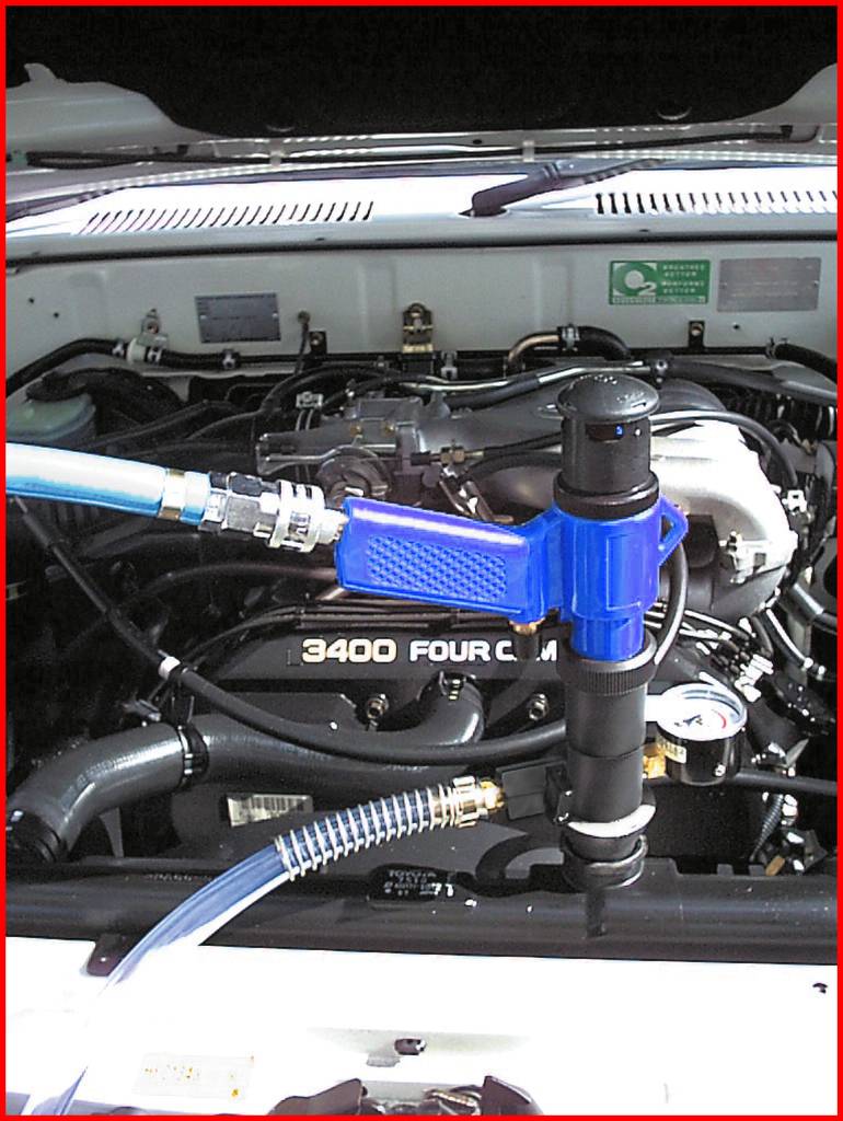 Motorruimte van een voertuig met een aangesloten blauw gereedschap. Het motorplaatje '3400 Four Cam 24' is zichtbaar.