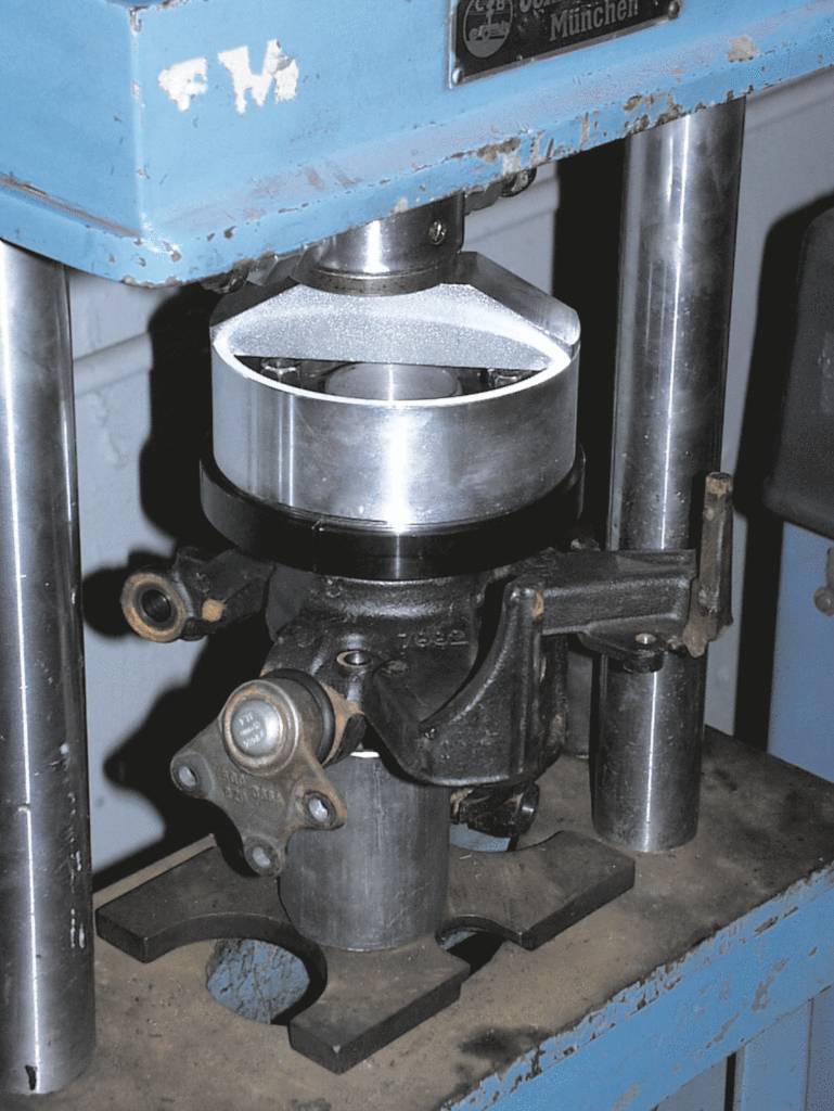 Een hydraulische pers in een werkplaats die een zilveren metalen stuk vormt.