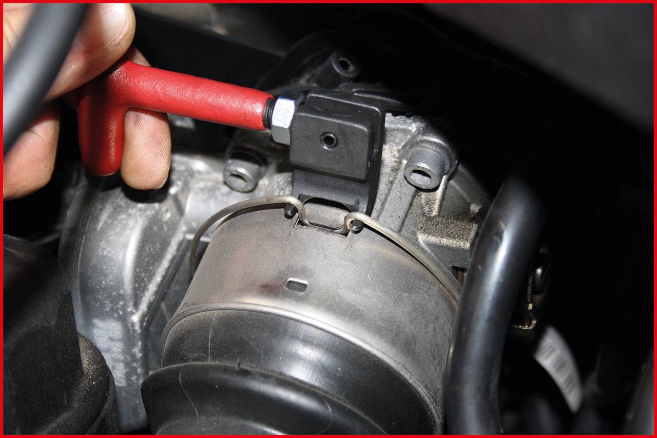 Een hand houdt een rood gereedschap vast bij een onderdeel van een motor. Op de afbeelding is de metalen behuizing van een motorcomponent zichtbaar.