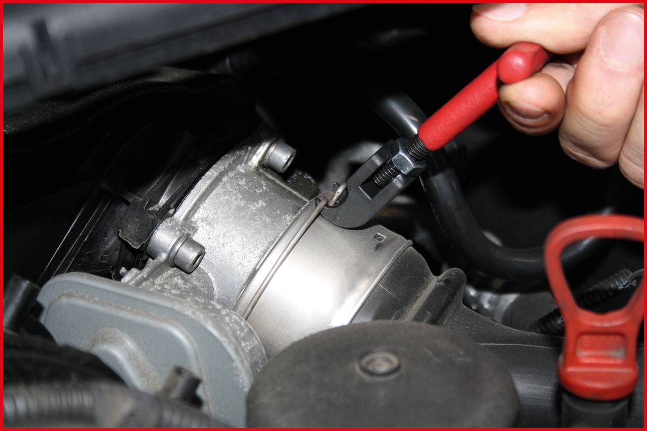 Hand houdt rode moersleutel vast om een klem aan een metalen buis in de motorruimte los te maken.