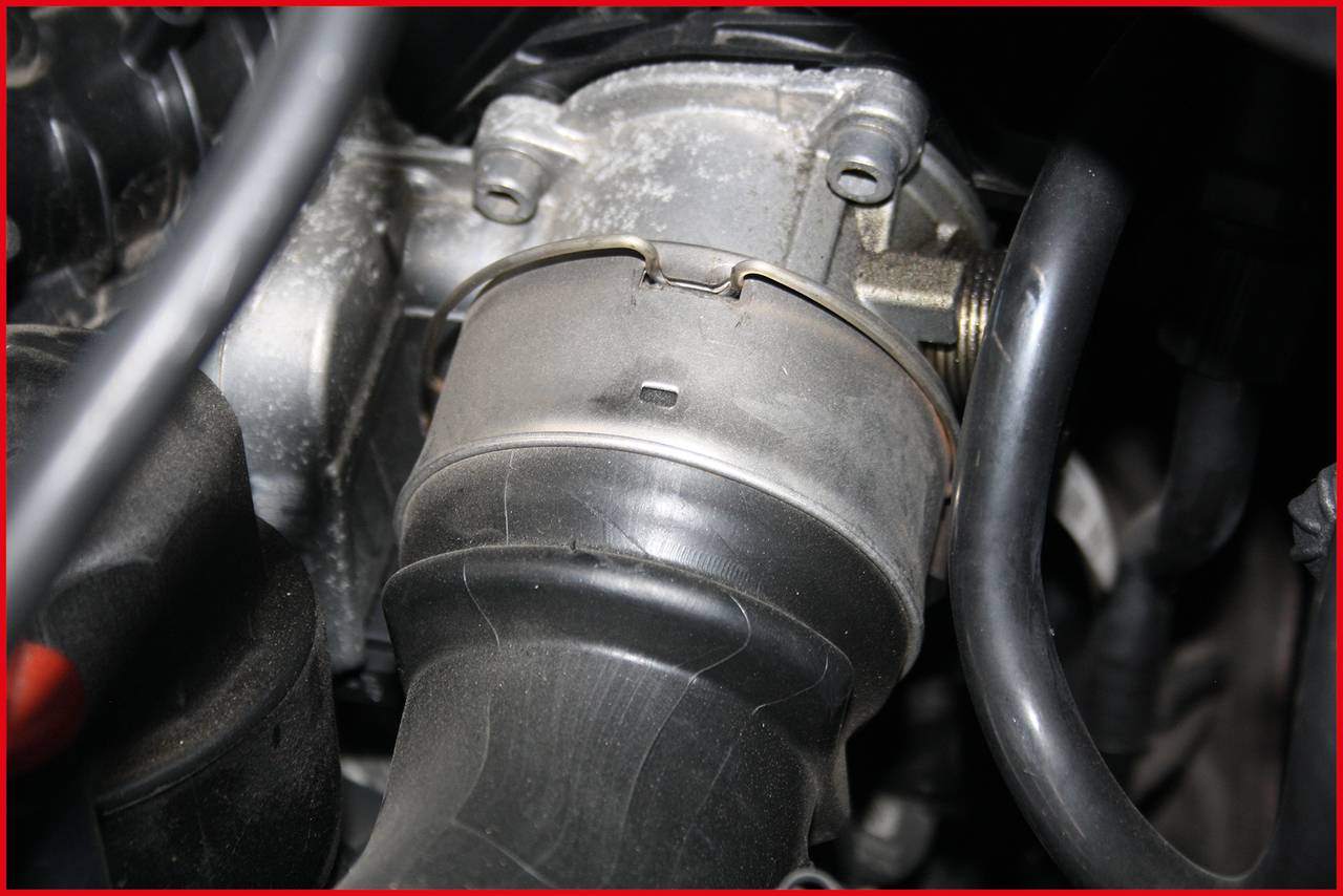 Een motorruimte met een close-up van een buisvormig onderdeel dat is aangesloten op een metalen component, vermoedelijk een onderdeel van het koelsysteem.