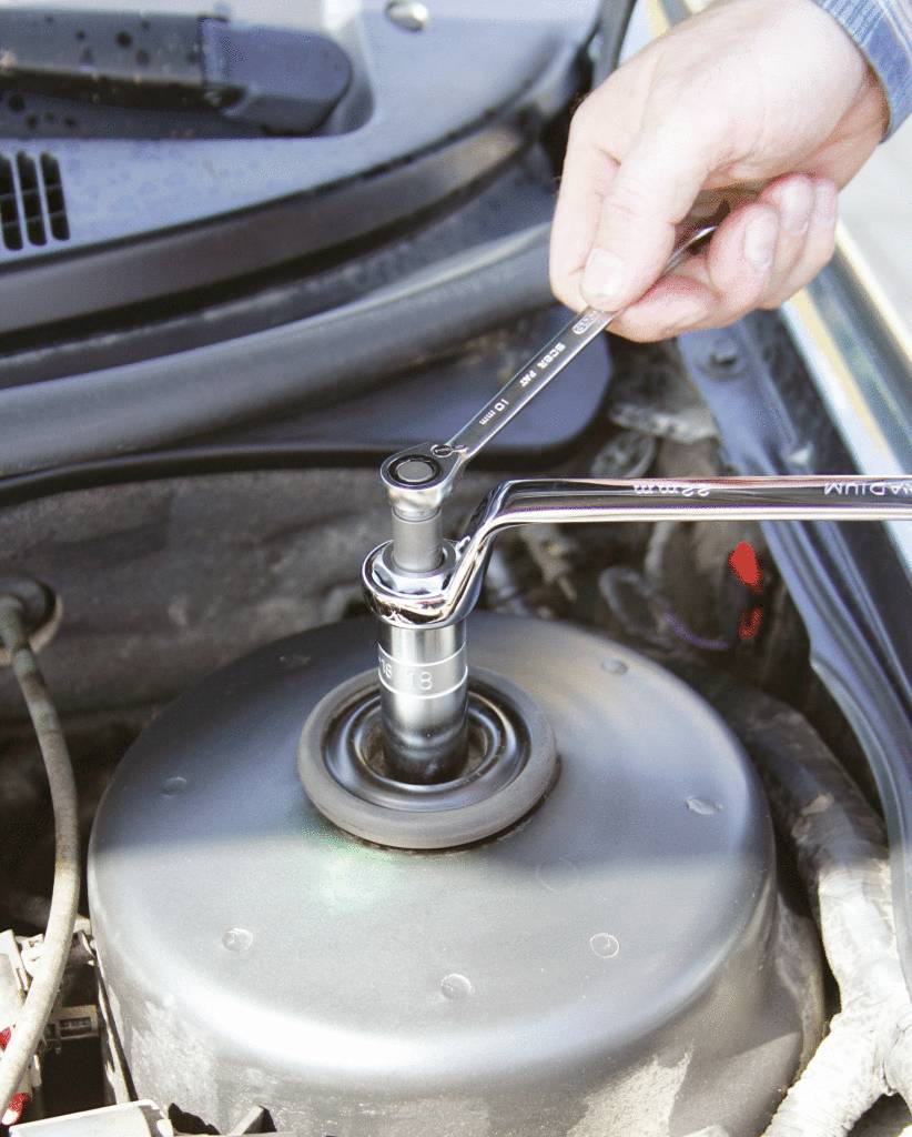 Een hand bedient een momentsleutel om een bout in de motorruimte van een auto vast te draaien.