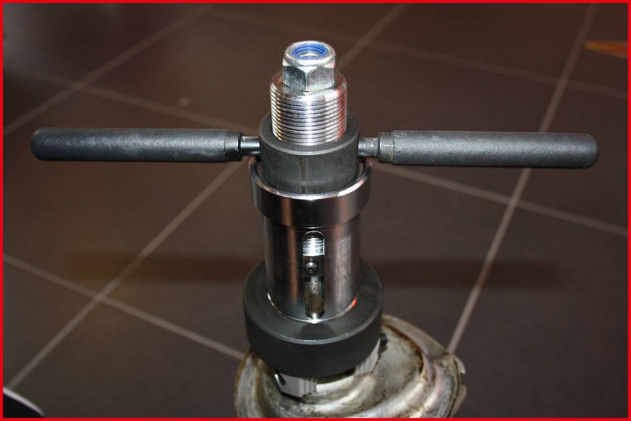 Een metalen gereedschap met handvatten en een schroefdraad, geplaatst op een tegelvloer. Het lijkt geschikt voor het snijden of vormen van buizen.