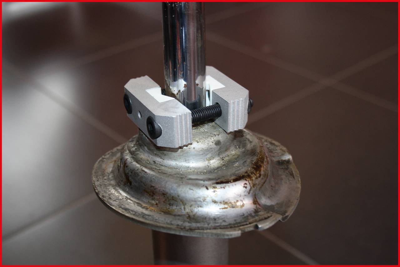 Close-up van een metalen staaf die is bevestigd met een schroefinrichting. Hij staat op een donker betegelde vloer.
