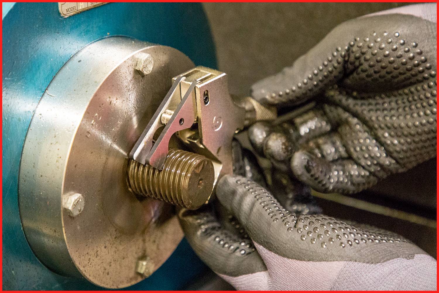 'Close-up van handen in werkhandschoenen die een metalen machine repareren of afstellen. Focus op precisiewerk.'