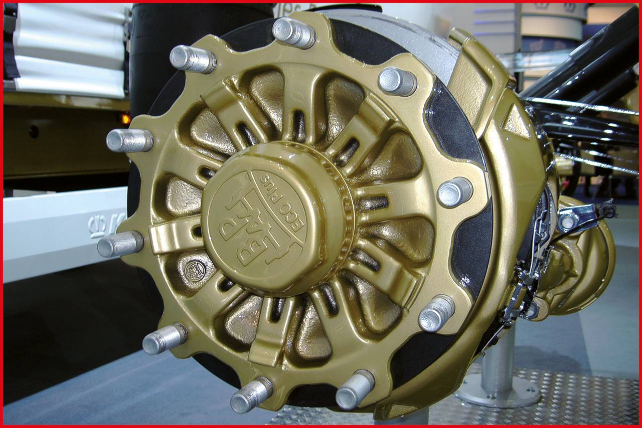 Close-up van een gouden vrachtwagen wielnaafmodule met acht schroeven, gemonteerd op een as in een industriële omgeving.