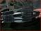 Een hand houdt een gereedschap vast om een wielmoer te verwijderen, dat over een as is geschoven. Reparatiescène in een werkplaats.