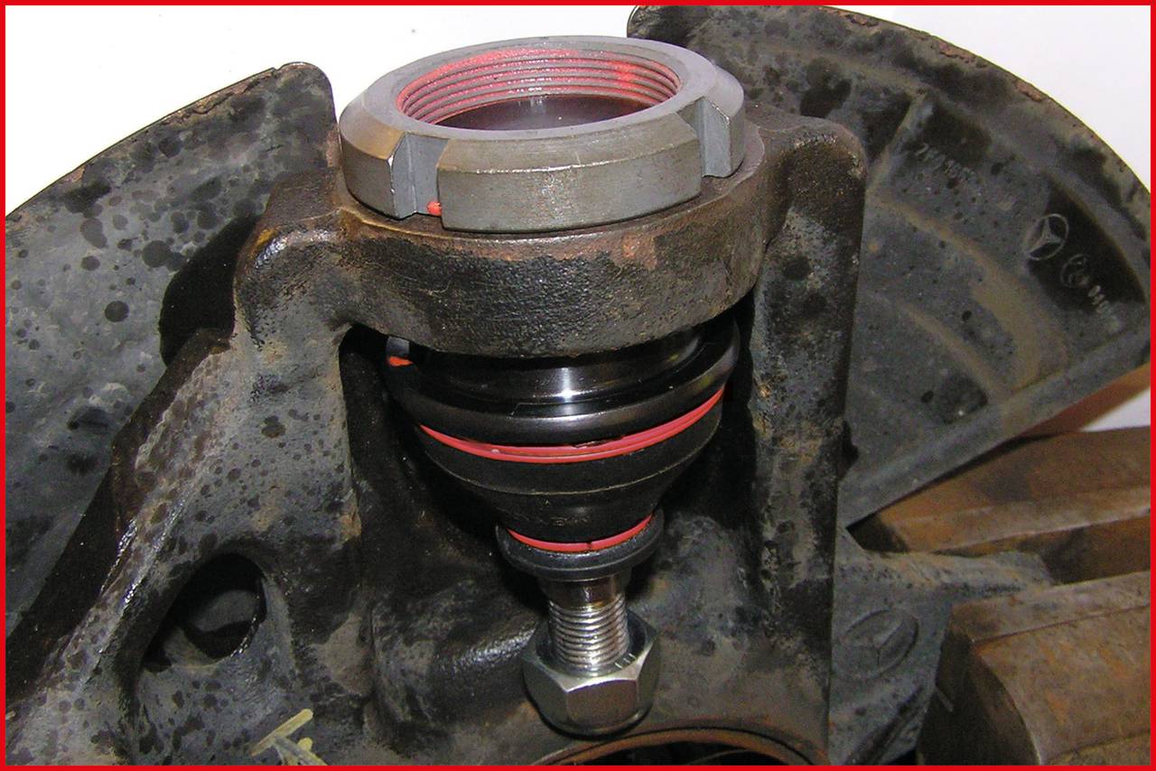 Close-upfoto van een mechanisch onderdeel met schroefdraad, mogelijk een kogelscharnier, bevestigd aan een metalen en gecorrodeerd element.