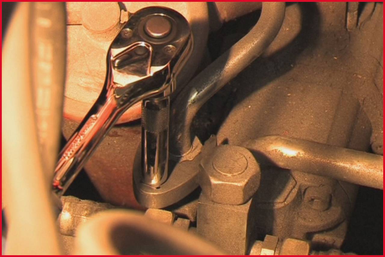 Een ratel wordt gebruikt om een schroef aan te halen in een motorruimte. Close-up toont mechanische details.