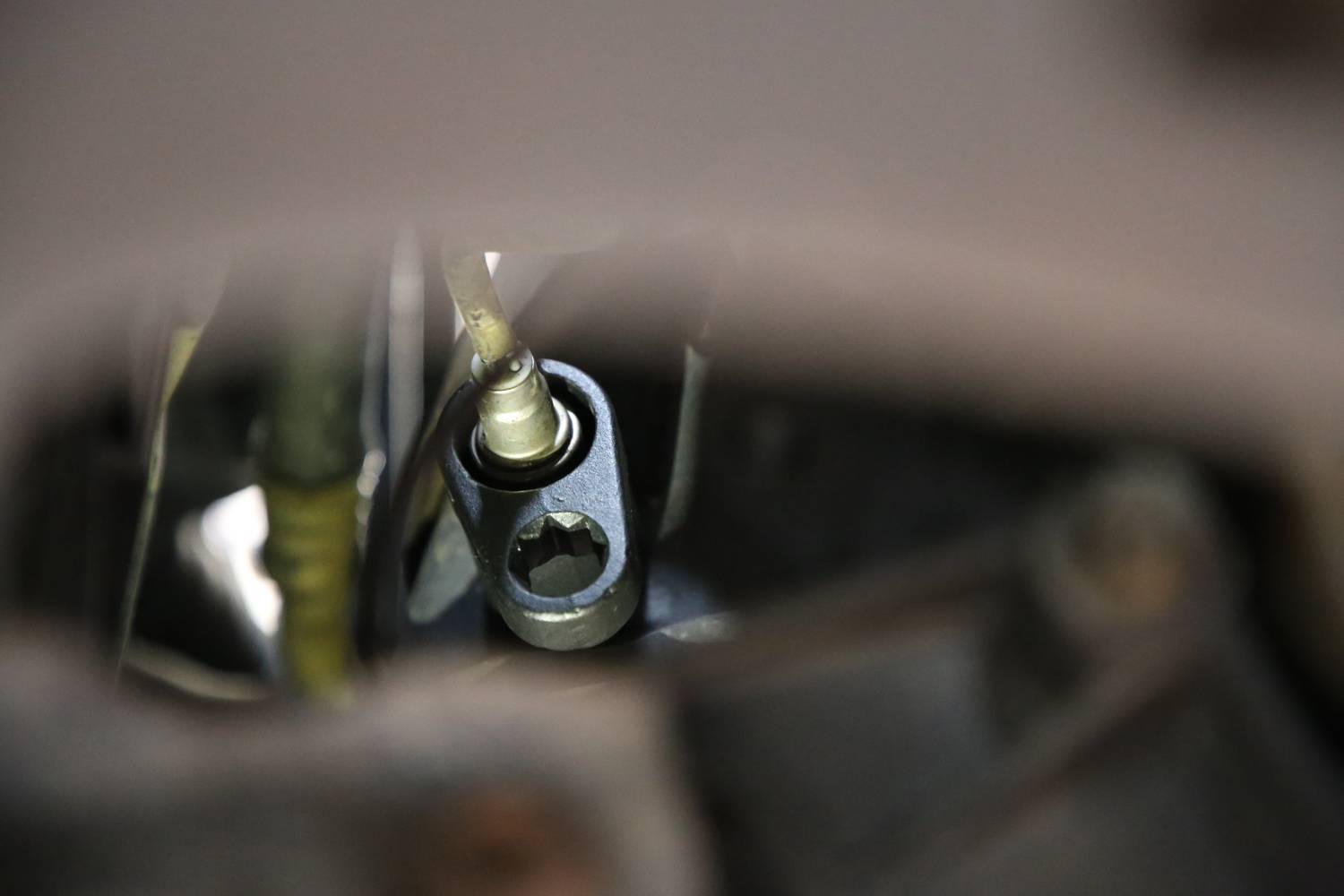 Een mechanisch onderdeel met een moersleutelaansluiting op een metalen houder, omgeven door kabels en metalen componenten in een machine.