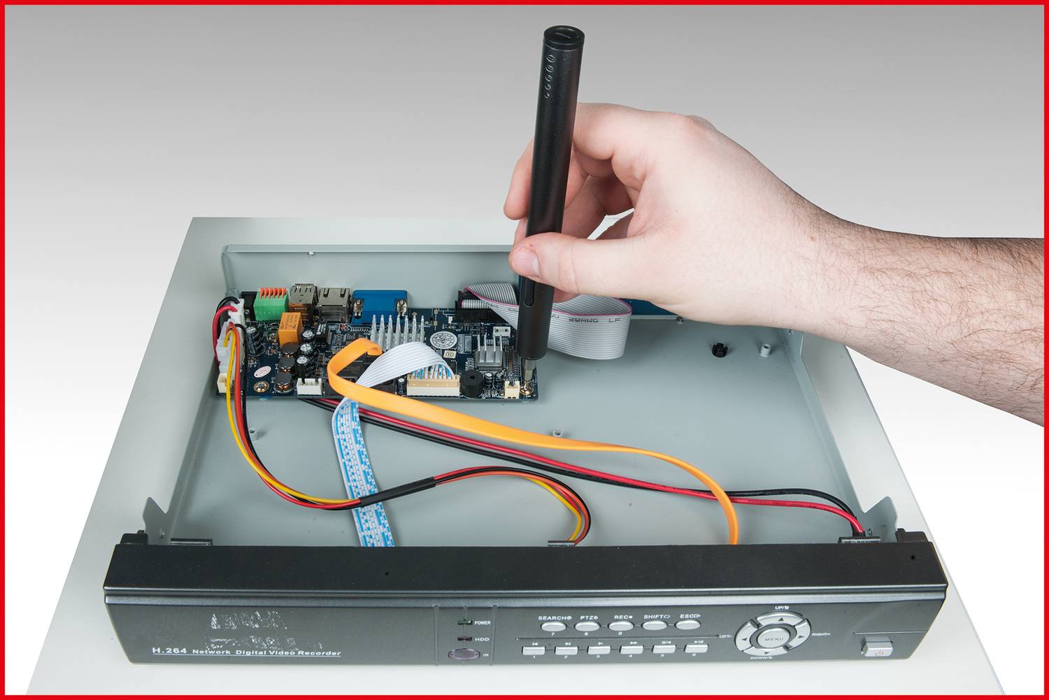 Een hand gebruikt gereedschap om te werken aan een open elektronische printplaat in een behuizing met zichtbare kabels en printonderdeelcomponenten.