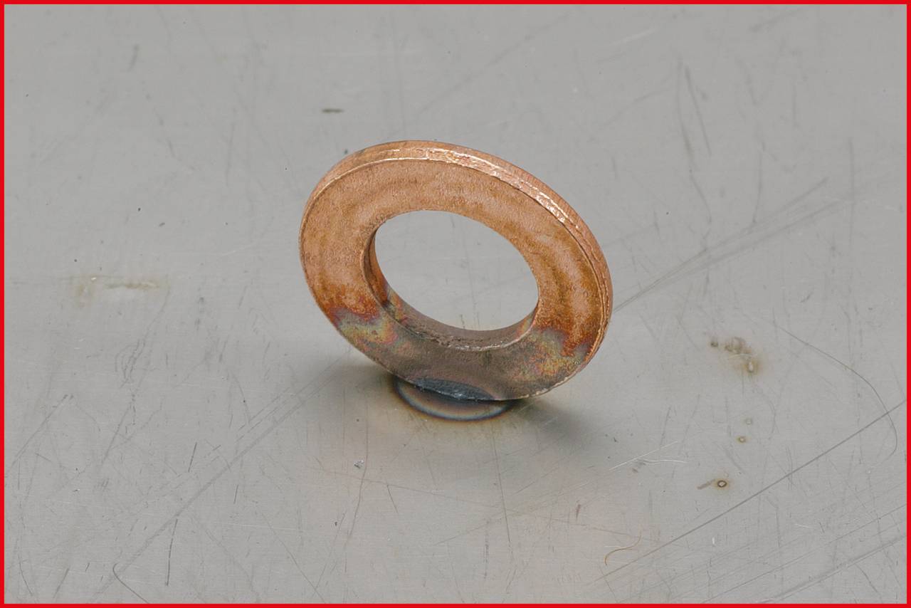 Een bronzen metalen sluitring ligt op een grijs gestructureerd oppervlak.