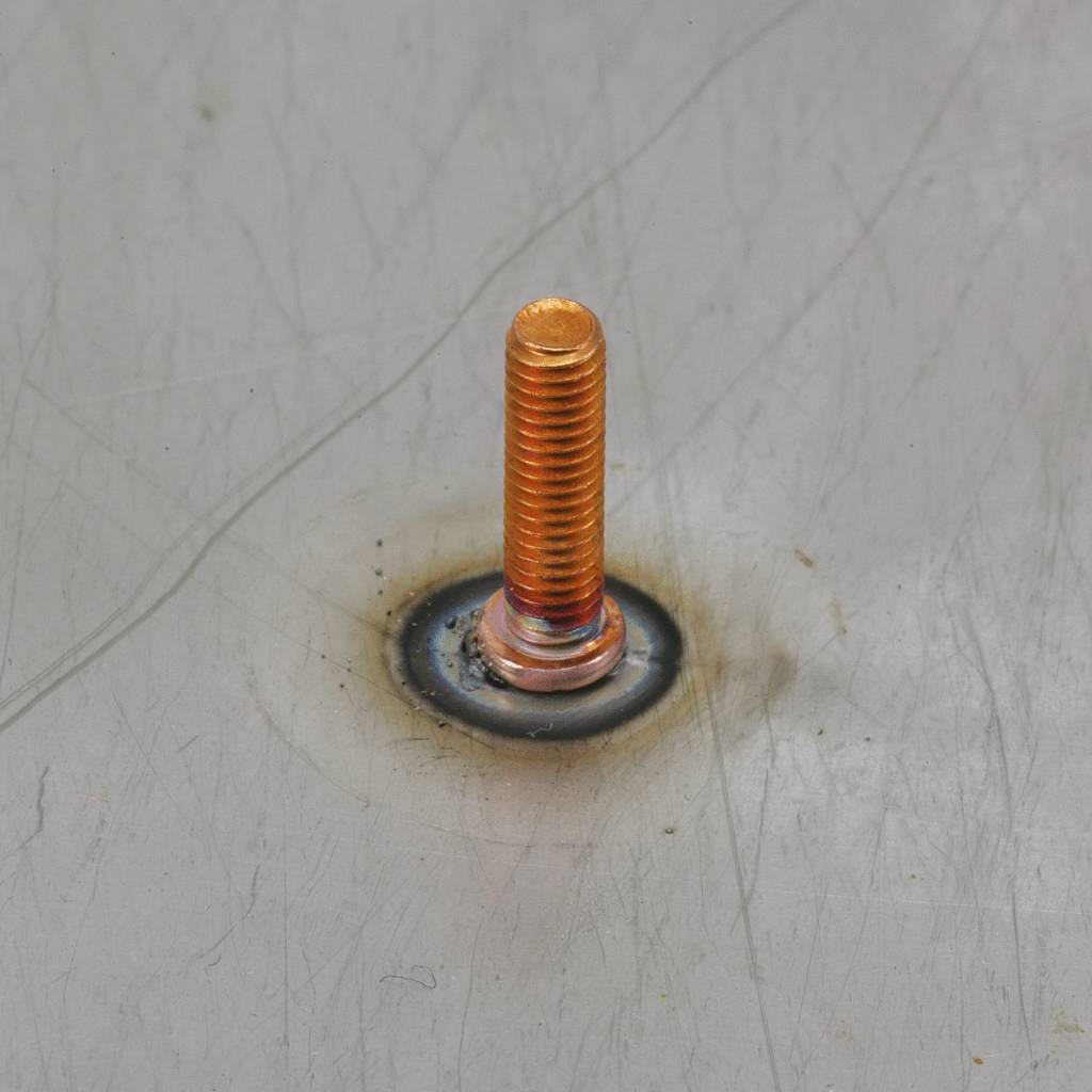 Een bout is op een metalen oppervlak bevestigd met een laspunt. De bout is oranje en contrasteert met het grijze metaal.