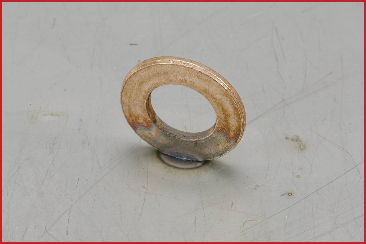 Een enkele metalen sluitring op een grijze ondergrond. De sluitring heeft een roestige, versleten uiterlijk.