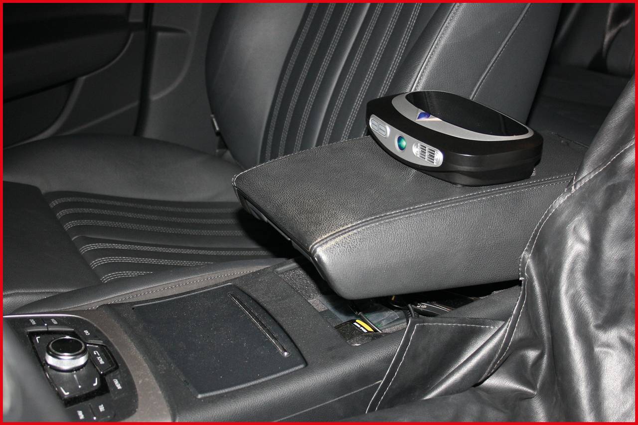 Een klein, zwart apparaat met een digitaal display op de middenconsole van een auto, vermoedelijk bedoeld voor het opbergen van voorwerpen.