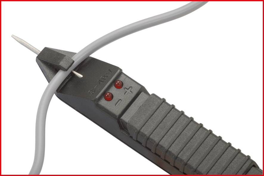 Een spanningzoeker ligt naast een grijs kabel. Twee rode lampjes zijn zichtbaar. De zoeker toont '12-48V'.