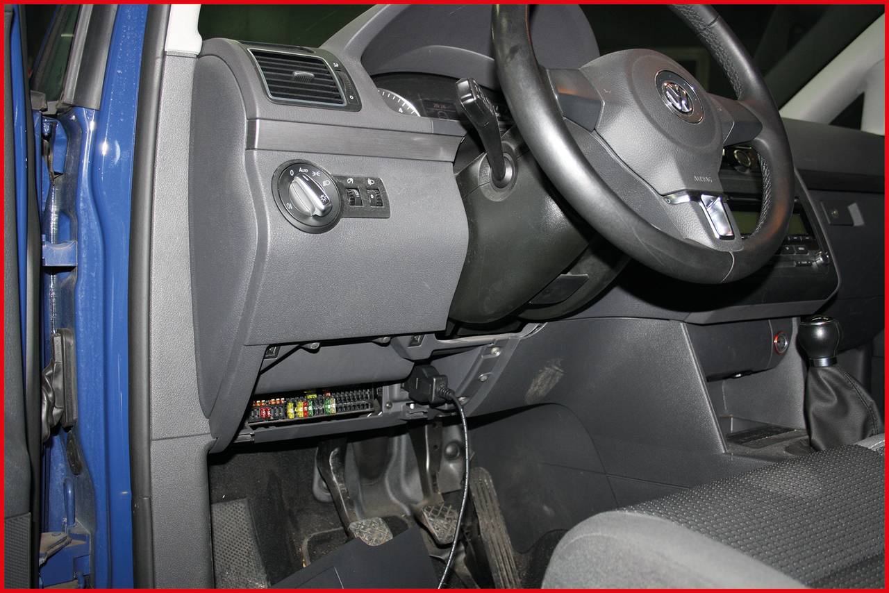 Interieur van een auto, met focus op het dashboard en het stuur. Een technisch apparaat is onder het stuur geïnstalleerd.