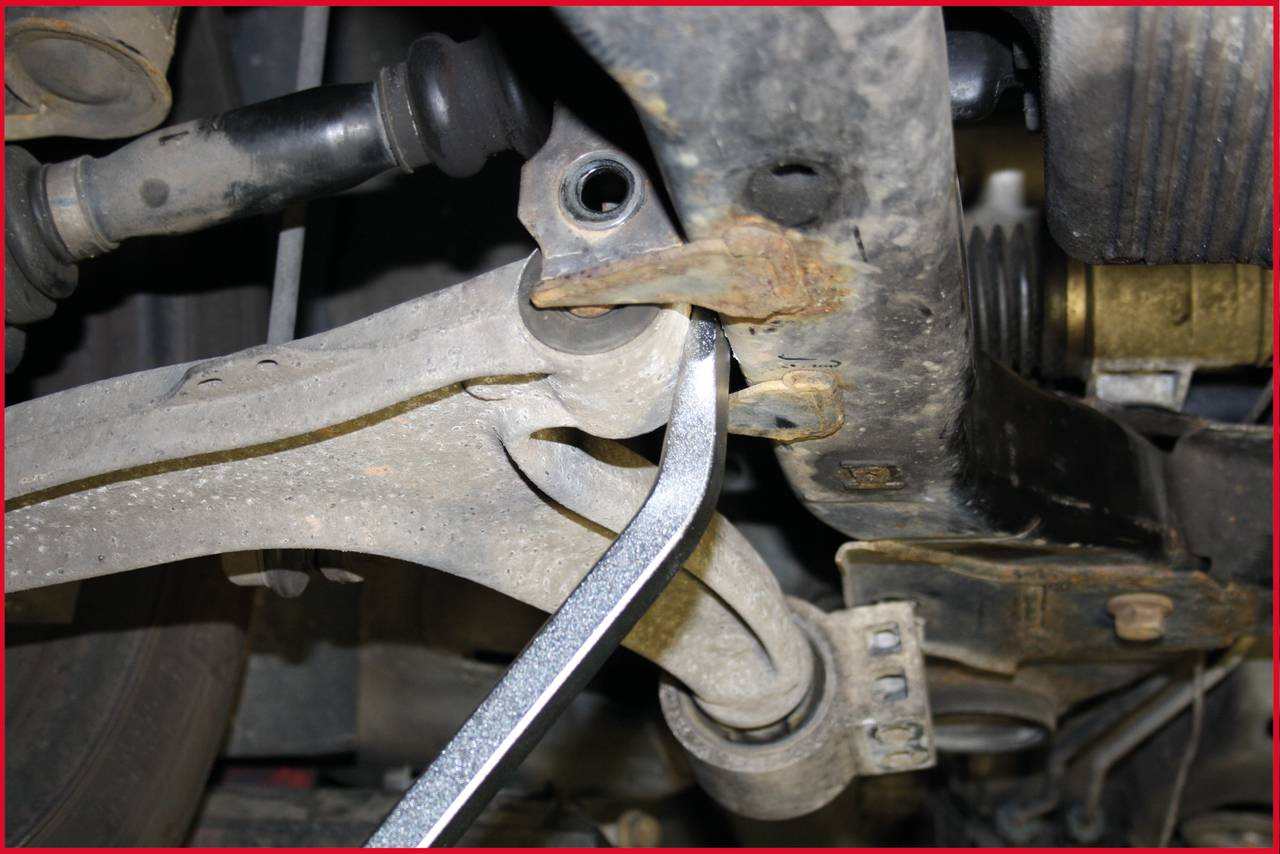 Een gereedschap draait een verroeste schroef vast aan de ophanging van een voertuig. De scène toont een reparatieproces.