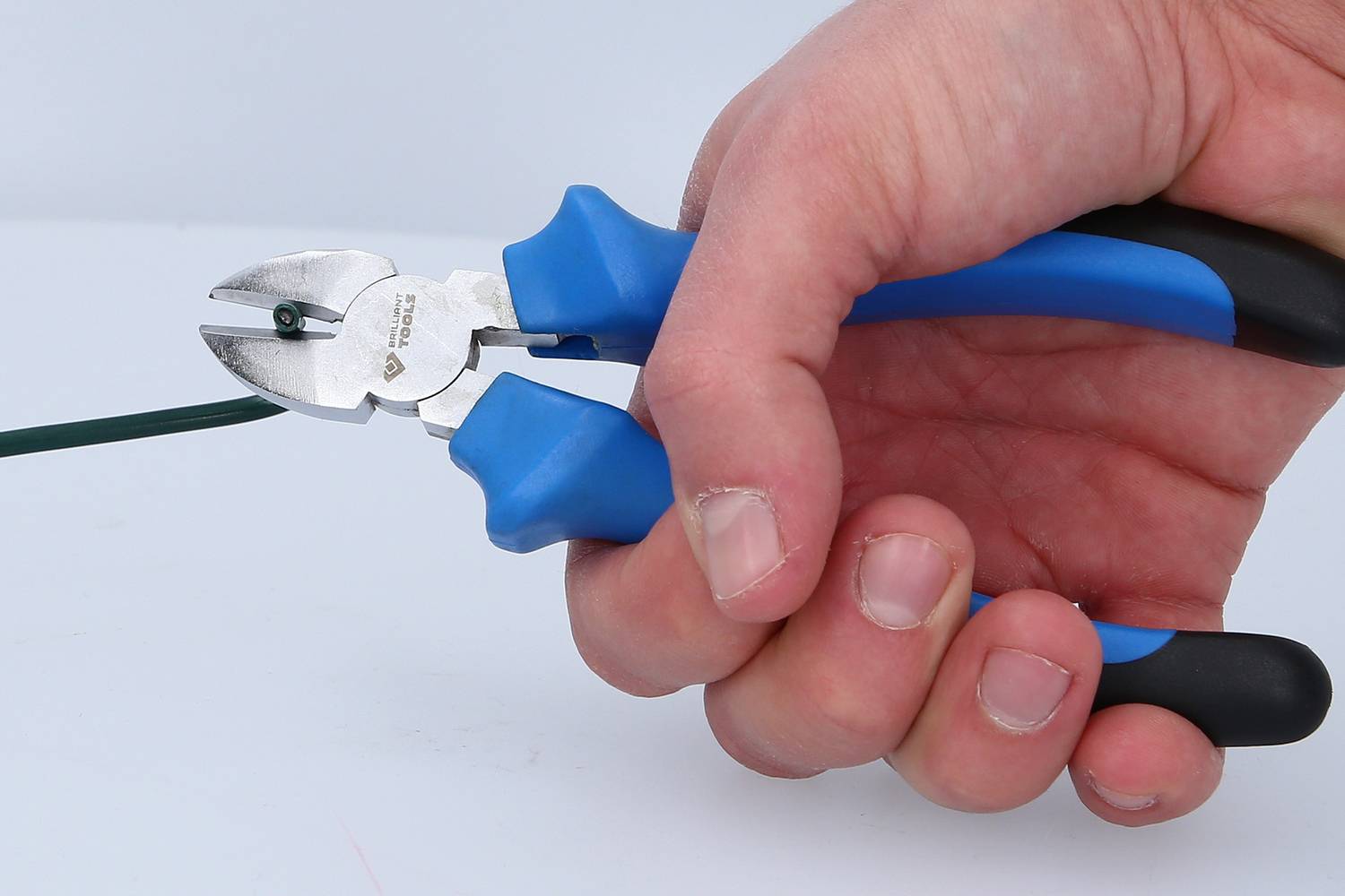 Een hand houdt een blauwe zijkniptang en knipt een groene draad door.