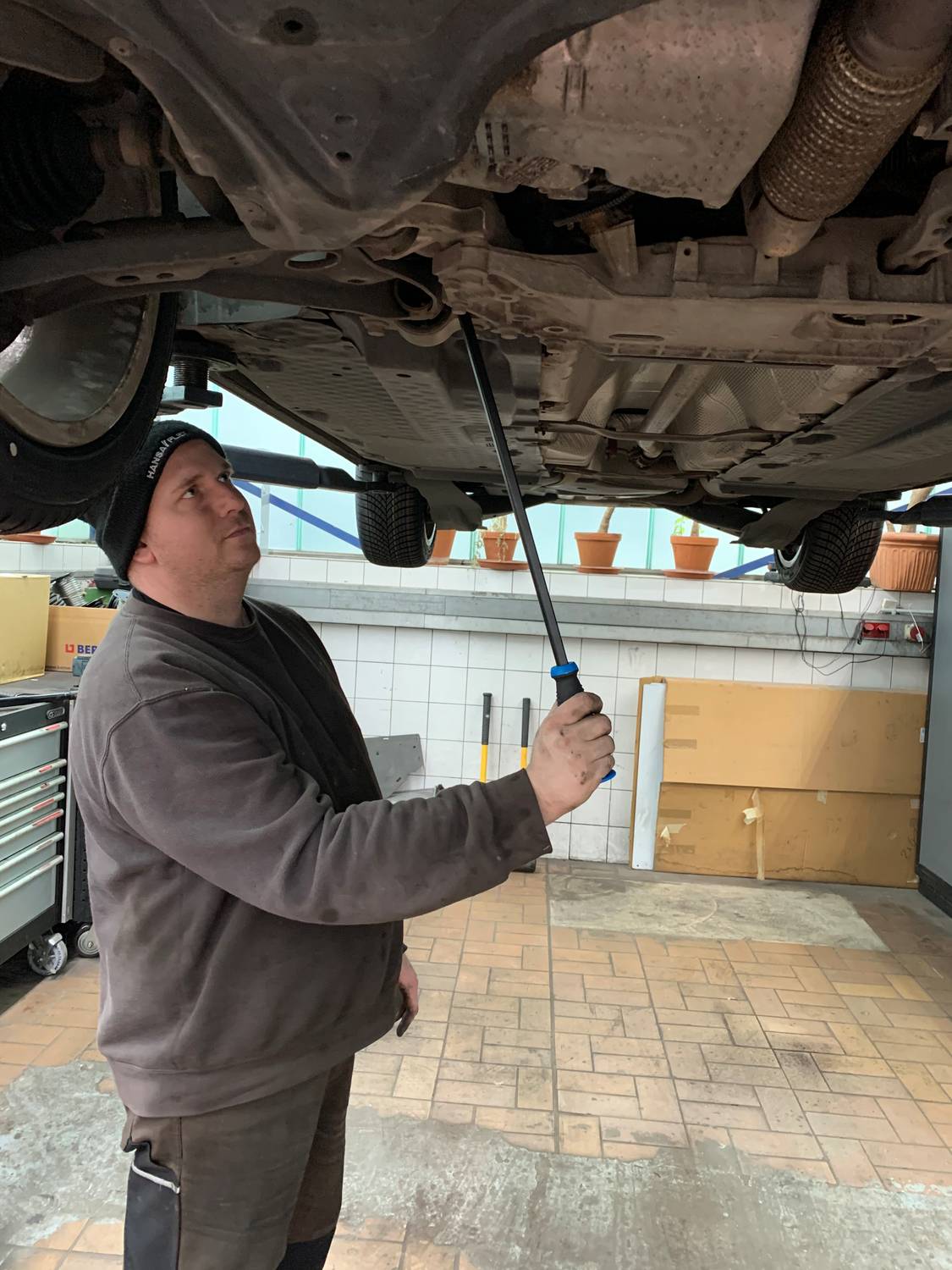 Een persoon inspecteert een auto die op bokken staat. Ze gebruikt een zaklamp om de onderkant van het voertuig te controleren in het autoservicegedeelte.