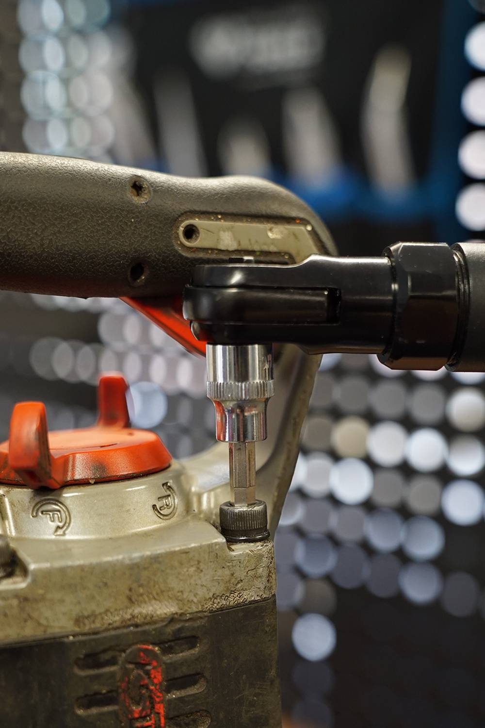 Een boormachine met een bruine handgreep en een zwarte opzetstuk wordt gebruikt om een schroef in een metalen behuizing te draaien. Achtergrond vervaagd.