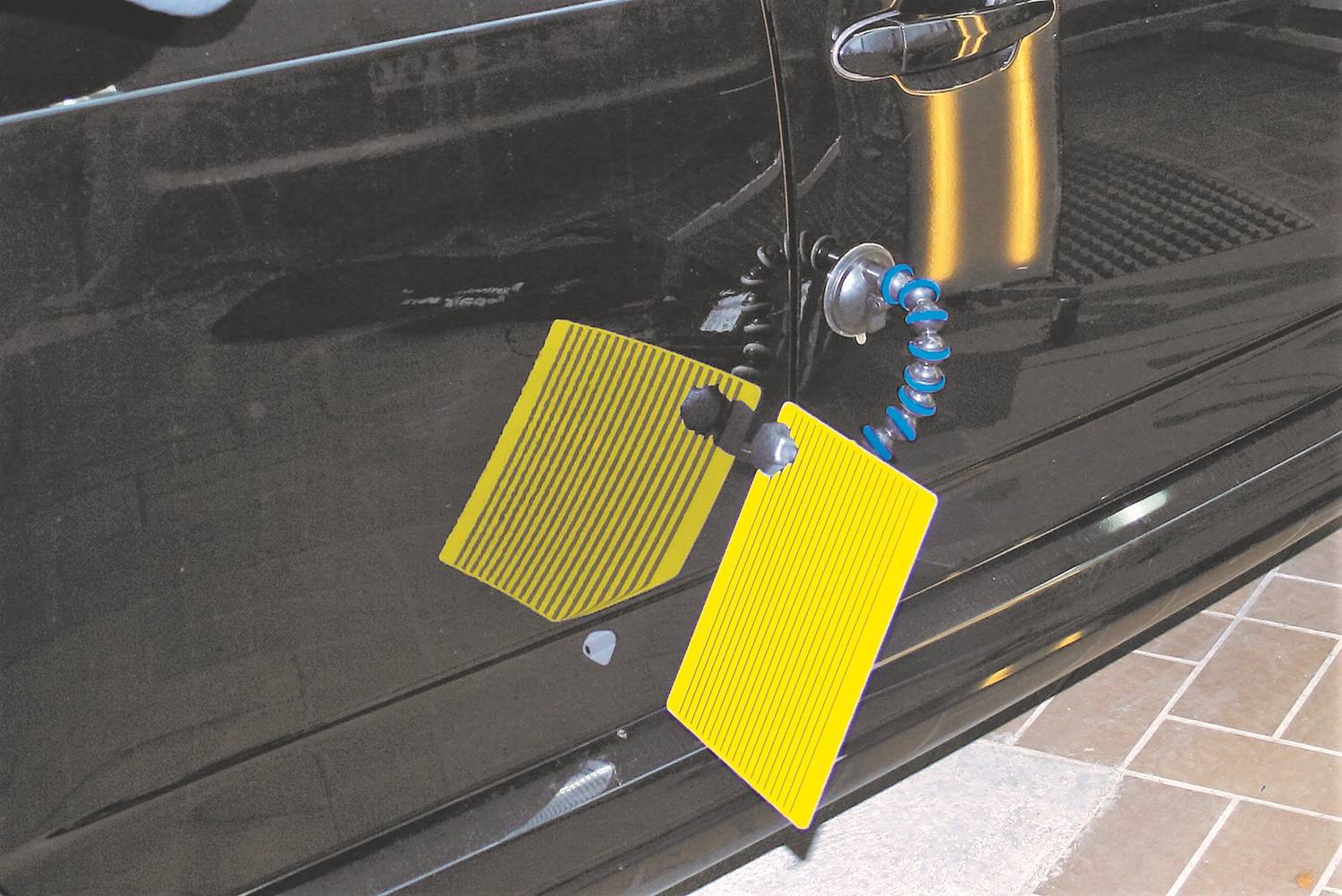 Een geel paneel met zwarte strepen wordt op een autoportier aangebracht om deuken zichtbaar te maken voor reparatie.