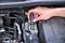 Een hand houdt een remvloeistoftester boven het reservoir in de motorruimte van een auto om de remvloeistof te controleren.