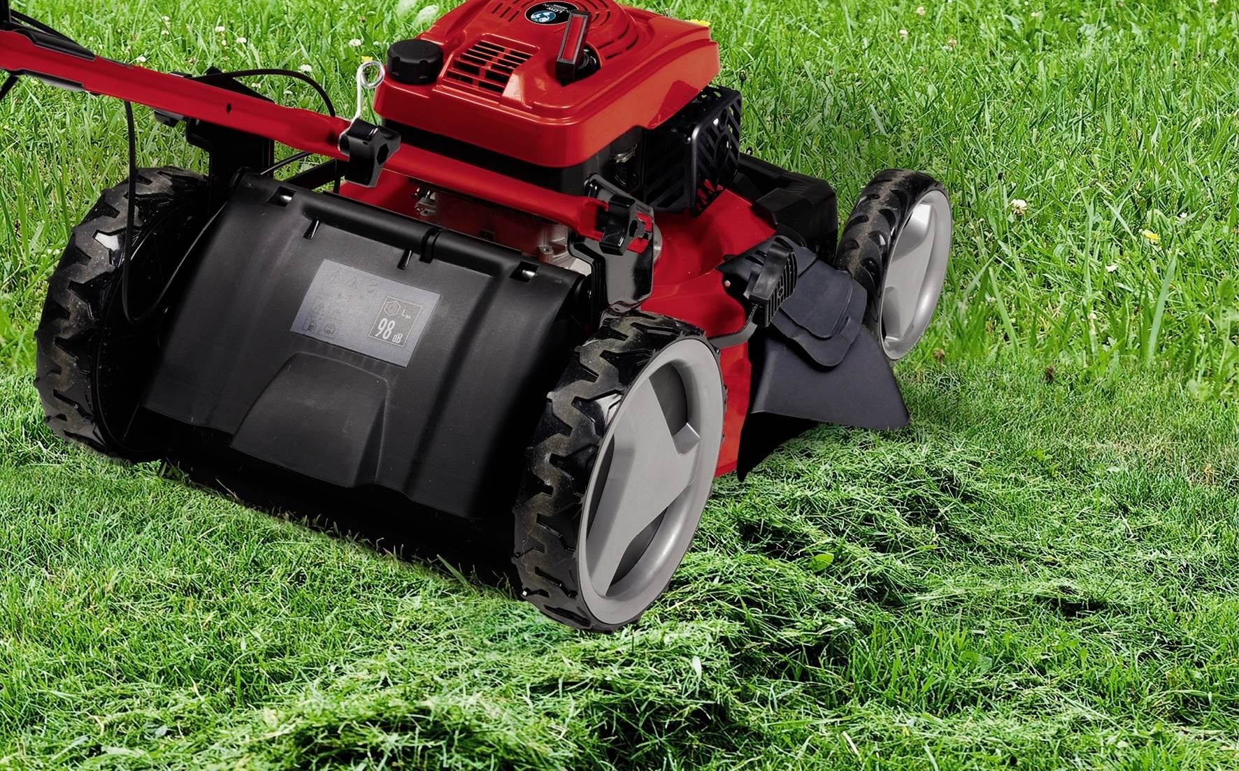 Een rode grasmaaier maait groen gras. Achteraan zijn de vers gemaaide grasstroken duidelijk zichtbaar.