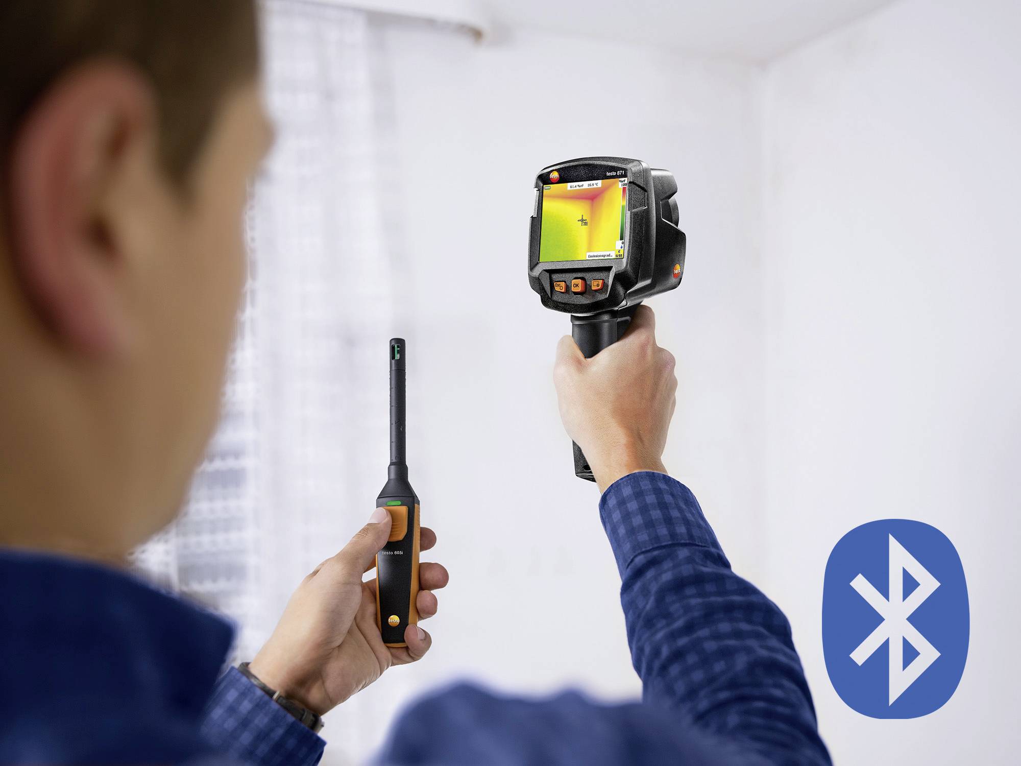 Een man houdt een warmtebeeldcamera en nog een meetapparaat vast. Op de achtergrond is een ruimte zichtbaar. Rechts staat het Bluetooth-symbool.