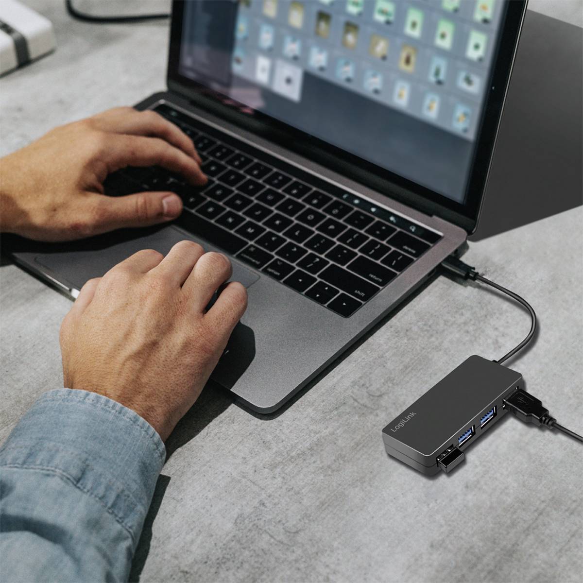 Persoon werkt op een laptop die verbonden is met een USB-hub; handen op het toetsenbord, hub heeft meerdere aansluitingen.