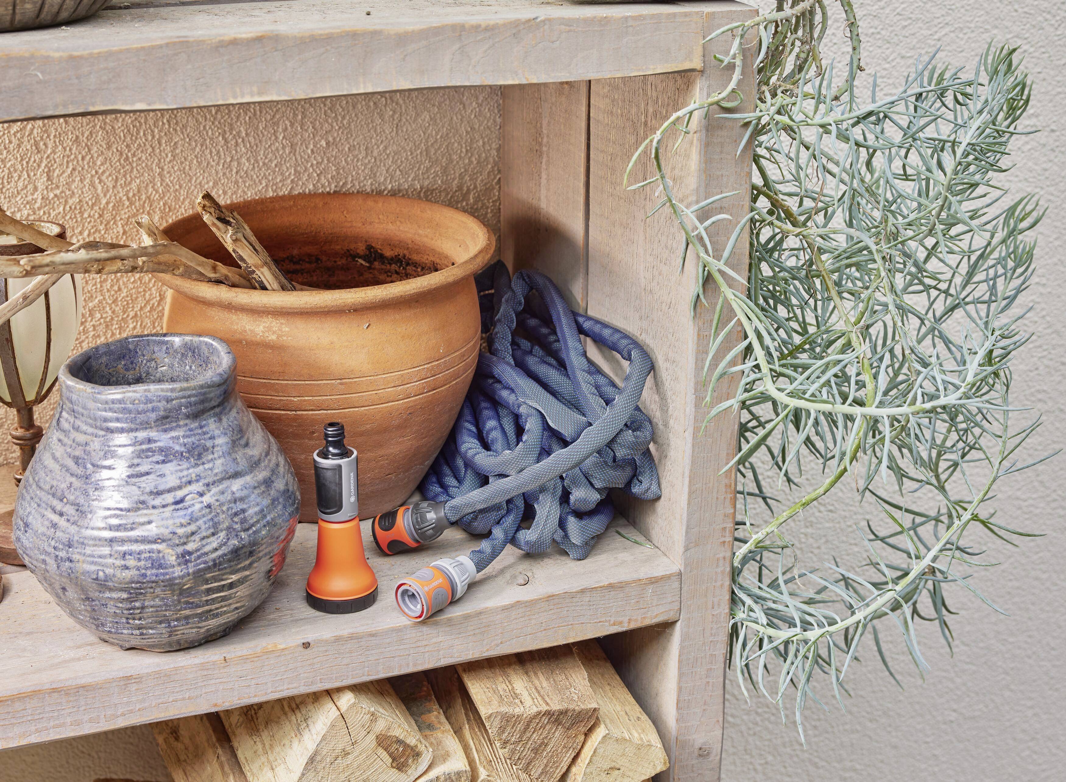 Rek met klei- en keramische potten, een sproeidop en een slang. Ernaast hangt een groen-grijze plant.