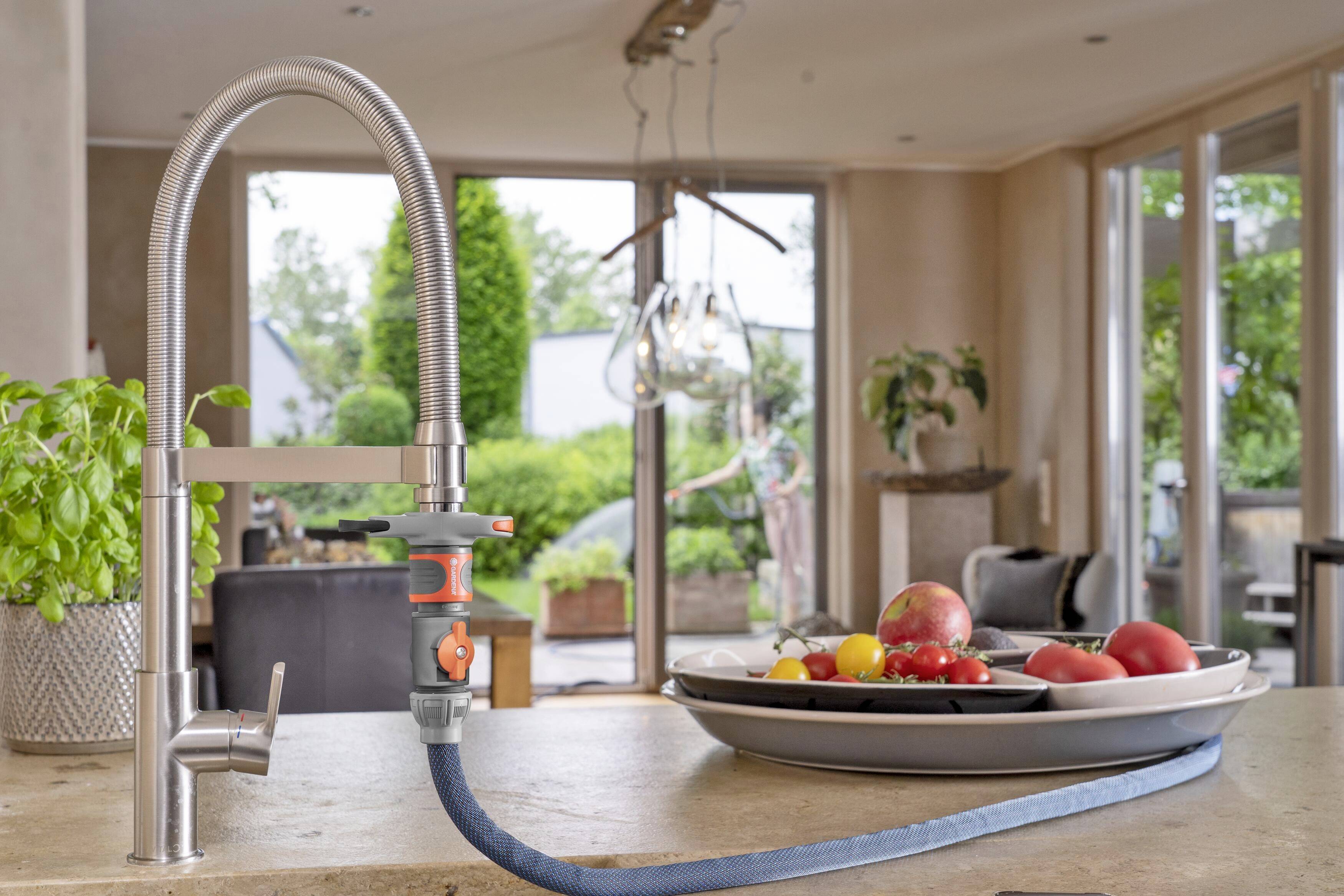 Een waterkraan in een moderne keuken met uitzicht op een tuin. Op het werkblad staan fruitschalen met appels en tomaten.