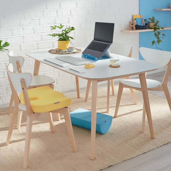 Een moderne, lichte ruimte met een tafel, stoelen, laptop en planten. Een gele kinderstoel op een stoel.