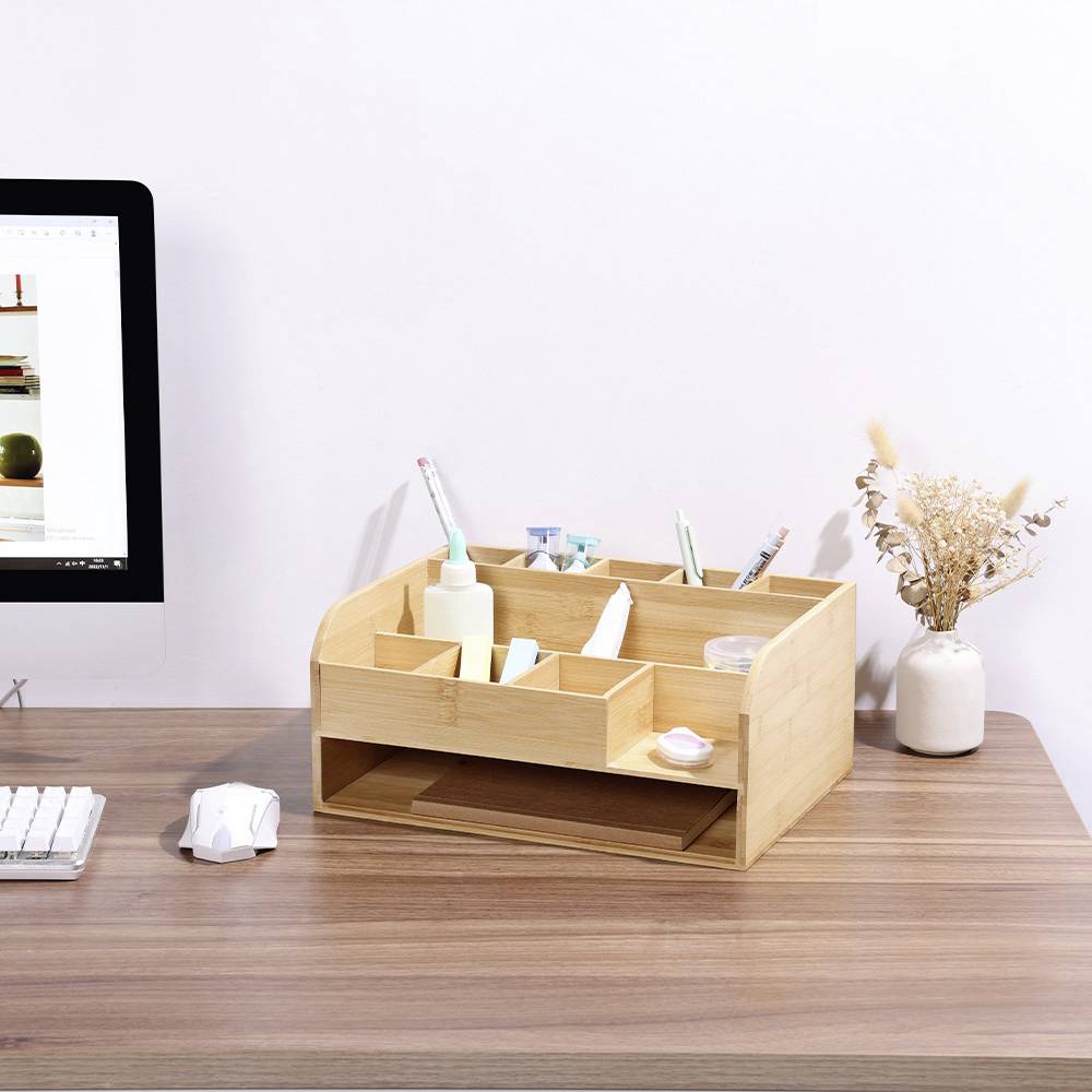 Houten bureauorganizer op een bureau met computer. Bevat pennen, plakband, schaar en notities. Ernaast een vaas met gedroogde bloemen.