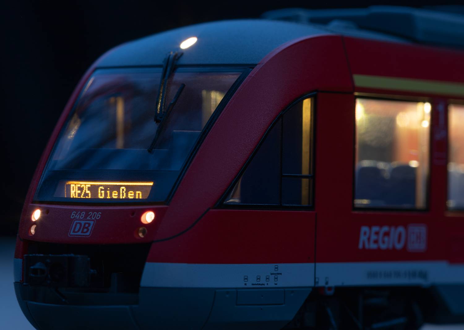 Een rode regionale trein van Deutsche Bahn met het opschrift 'RE25 Gießen' schittert in het donker.