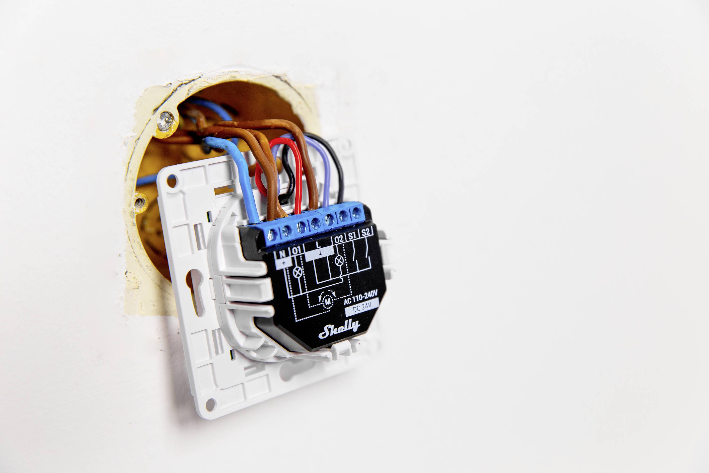 Een open wandschakelaar met meerdere gekleurde kabels die zijn aangesloten op een elektrische module; toont elektrische installatiewerkzaamheden.