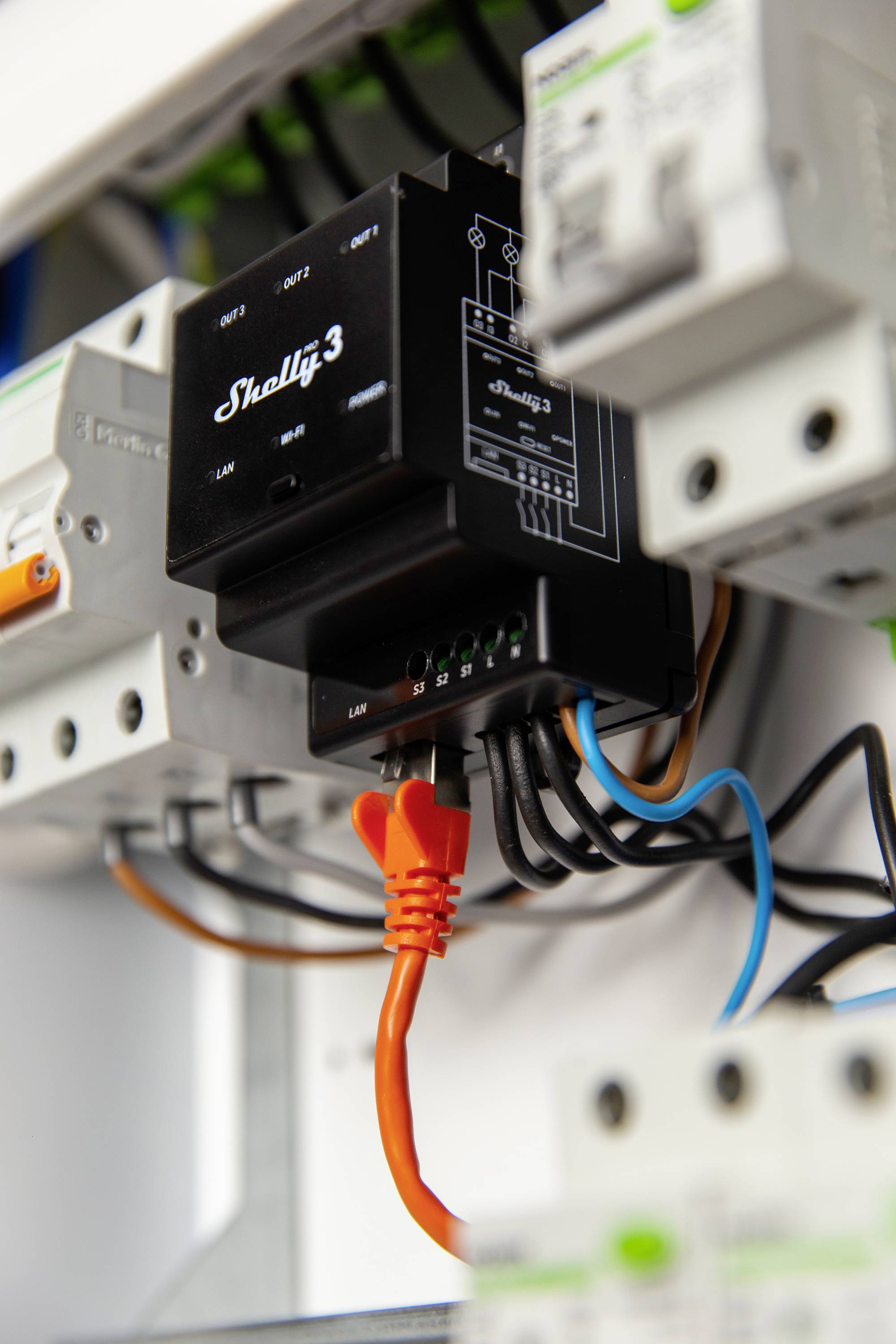 Een zwart elektronisch apparaat met het opschrift 'Shelly 3' is aangesloten op andere elektrische componenten. Een oranje kabel steekt eruit.