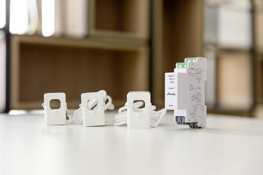 Drie witte, vierkante sensoren met kabels staan op een tafel naast een grijs elektrisch apparaat. Achtergrond onscherp.