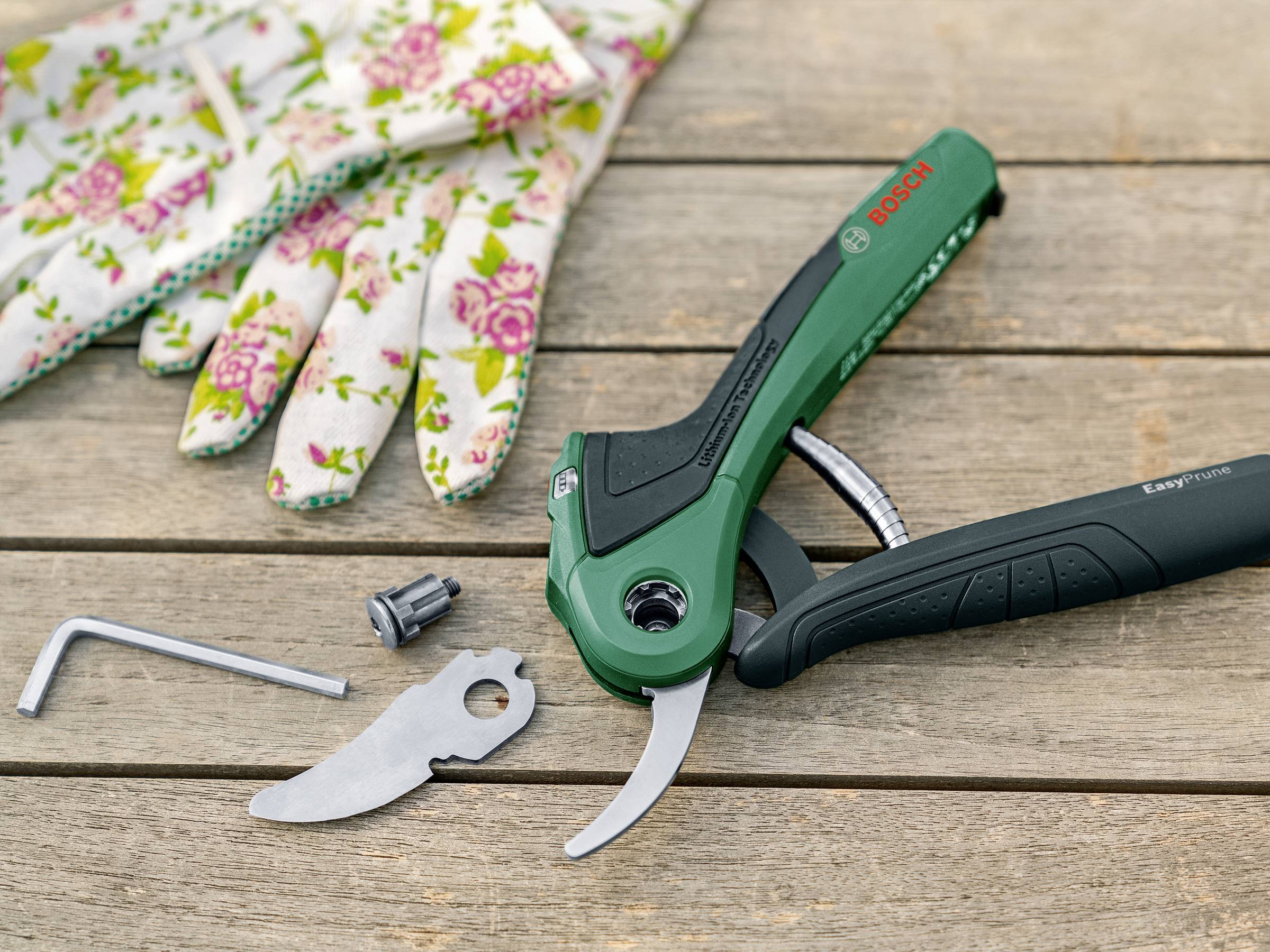 Tuinschaar met reserveonderdeel en moersleutel op houten tafel, naast een paar tuinhandschoenen.