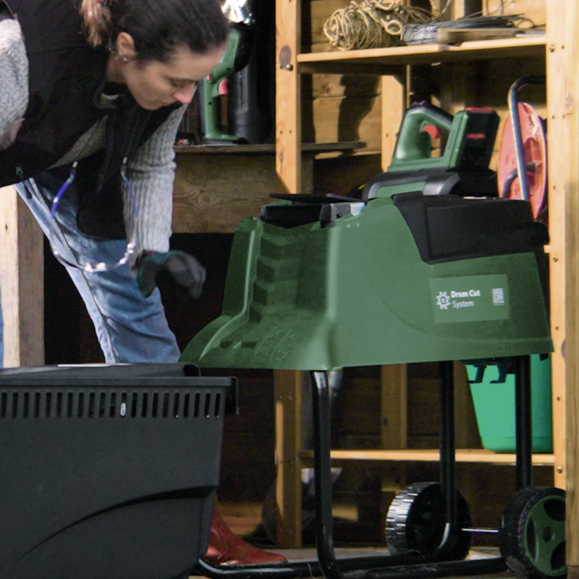 Een persoon werkt in een schuur aan een groene bladblazer. Op de achtergrond zijn gereedschappen en houten rekken te zien.